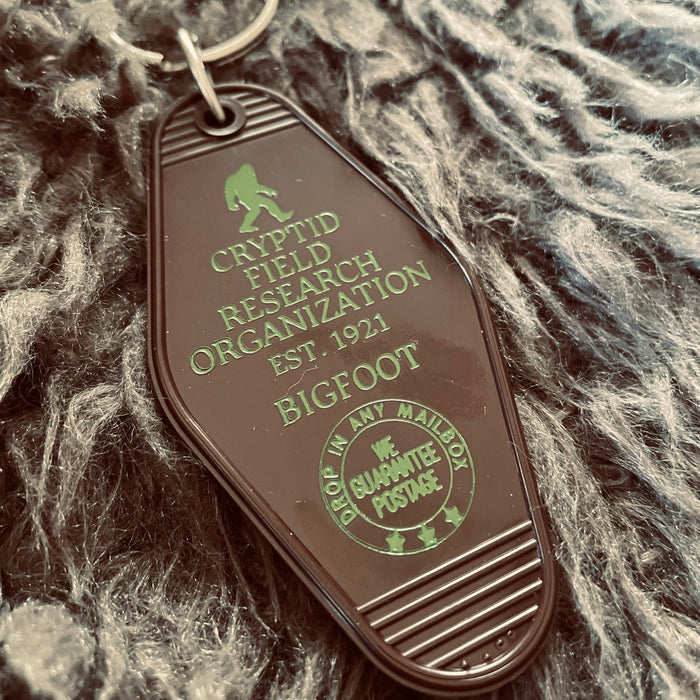 Forager Provisions LTD vintage-style plastic motel key fob featuring a green Bigfoot Cryptid Field Research Org design.