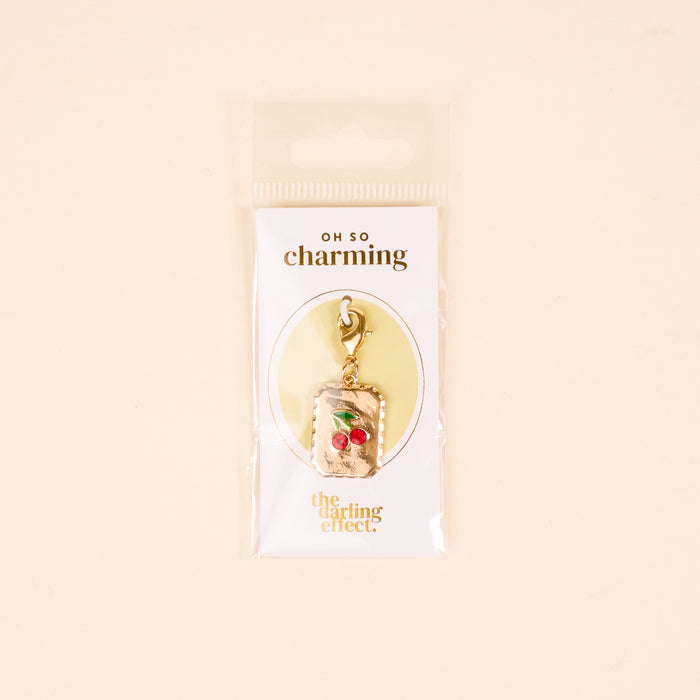 Add a playful touch to your jewelry with The Darling Effect's "A Cherry Moment Jewelry Charm Gold," featuring two red cherries on a stem and lobster clasp. Arrives on a white card with OH SO charming and The Darling Effect branding.