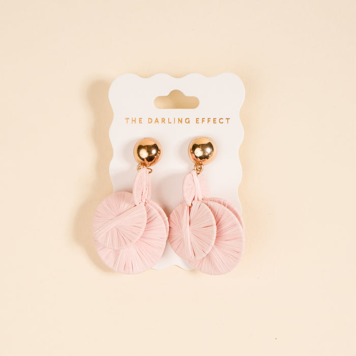 Blush Pretty and Polished Earrings by The Darling Effect feature light pink circular, textured designs on shiny gold studs. Lightweight and ideal for daily wear, they're shown on a branded white card against a beige background.