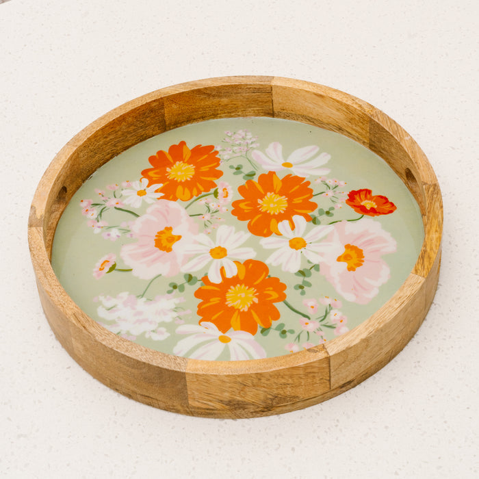 The-darling-effectβs Bouquet Beauty Sage Large Round Wood Enamel Tray features orange, white, and pink floral designs on a light green background, displayed on a white surface.