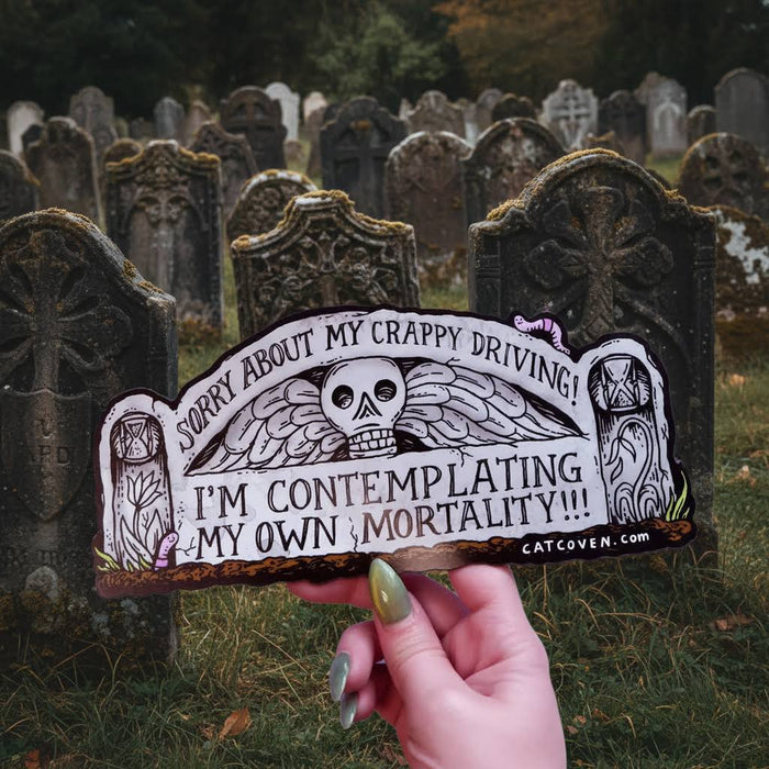 Forager Provisions LTD Cat Coven Mortality car magnet with gothic skull design held in front of a graveyard.
