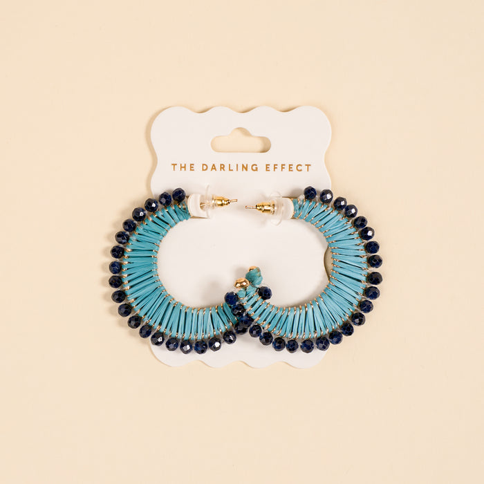 The Darling Effect’s Coastal Blue It-Girl Earrings—blue and navy beaded boho earrings—are shown on a branded card against a beige background. These lightweight earrings are perfect for everyday wear.