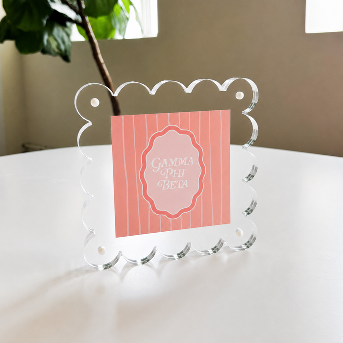 The Darling Effect’s Gamma Phi Beta Square Scalloped Acrylic Frame showcases a pink, vertically striped “Gamma Phi Beta” card in white script—a chic, modern accent for your space.