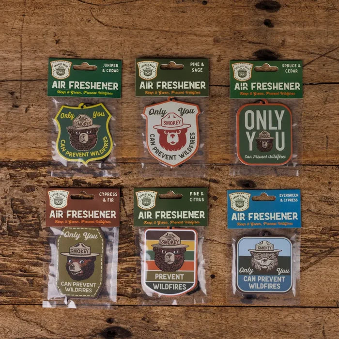 Six Good & Well Supply Co Smokey Bear Pine & Sage car air fresheners displayed neatly on a rustic wooden table.