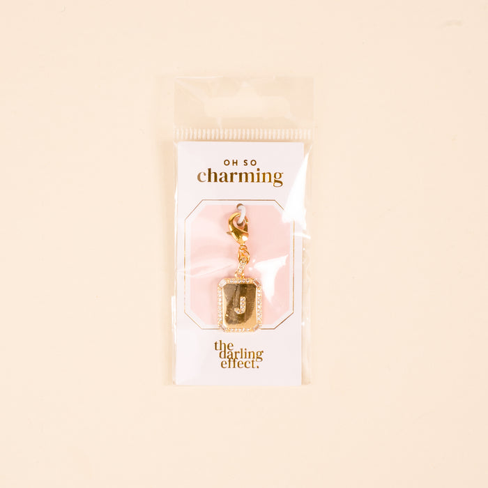 The-darling-effect J Jewelry Charm Initial Letter Gold features a gold-plated brass "J" with a glitter border, clasp, and is displayed on a branded card in clear packagingβperfect personalized jewelry on a cute pink-and-white background.