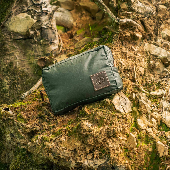 Forager Provisions LTD Journeyman Craft green waxed canvas expedition pouch resting on a mossy forest tree stump.