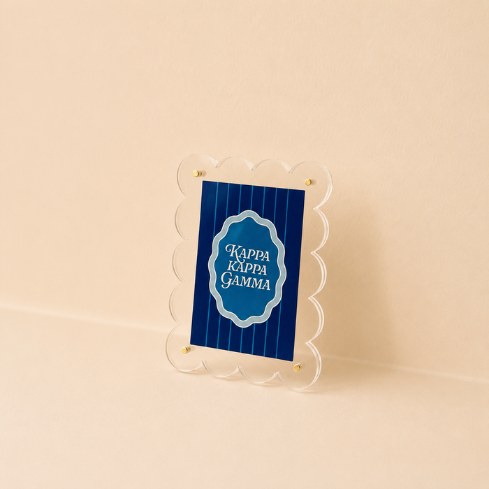The Darling Effect Kappa Kappa Gamma Mini Acrylic Picture Frame Magnet features a scalloped-edge clear frame holding a blue sign with white text, displayed on a beige background.