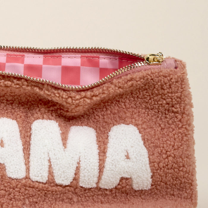 A close-up of the-darling-effect's Mama 2.0 Teddy Pouch shows its fuzzy pink sherpa exterior with white "MAMA" letters and an open view revealing a pink and white checkered ultra-soft lining.