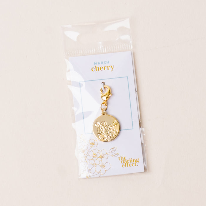 The-darling-effect's March Jewelry Birth Flower Charm Gold features a cherry blossom design attached to a "March cherry" card, presented in a clear plastic pouch on a light background.