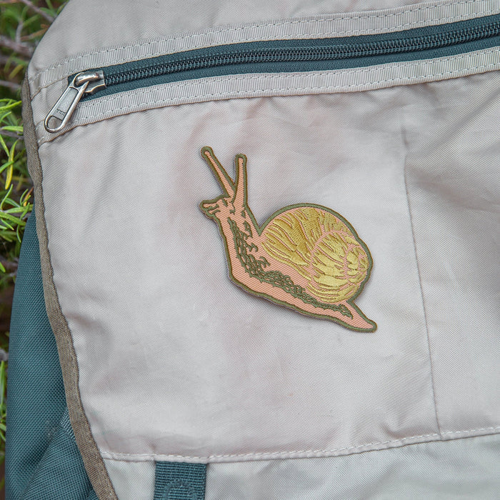 Forager Provisions LTD Mustard Beetle embroidered snail iron-on patch attached to a beige canvas backpack