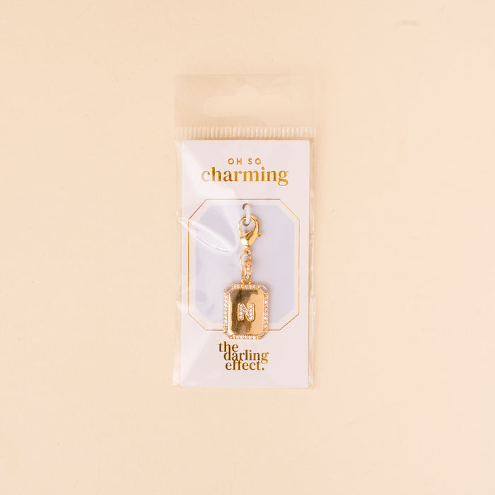 The-darling-effect N Jewelry Charm Initial Letter Gold features a gold-plated brass M encrusted with small gems and a lobster clasp, displayed on an OH SO charming card in clear packaging.