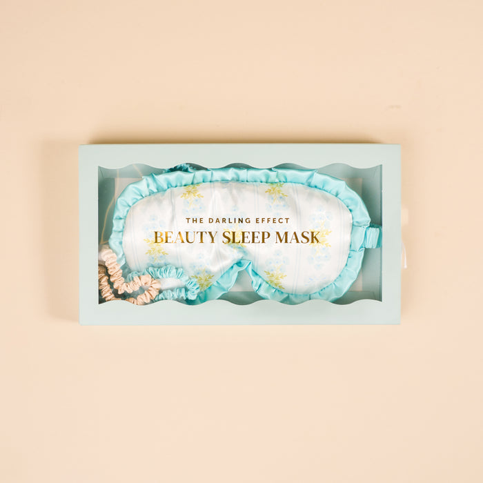 The Darling Effect Oh So Fancy Blue Beauty Sleep Mask gift box features a floral satin sleep mask with ruffled trim and two mini satin scrunchies in blue and nude shades.