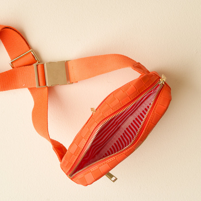 The Darling Effectโs Orange Urban Check Belt Bag features vegan leather, a gold buckle and zipper, and a red-and-white striped liningโshown open against a light beige background for a stylish, versatile accessory.