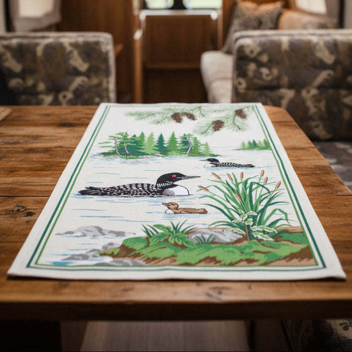 Forager Provisions LTD PAINE’S cotton kitchen towel featuring a rustic loon lake illustration on a wooden table.