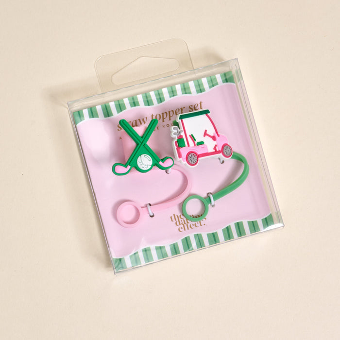 The Darling Effect Par-tee Pack Straw Topper Set includes two silicone toppersβone shaped like crossed golf clubs with a ball, the other a pink golf cartβon a pink and green striped card in a clear box.