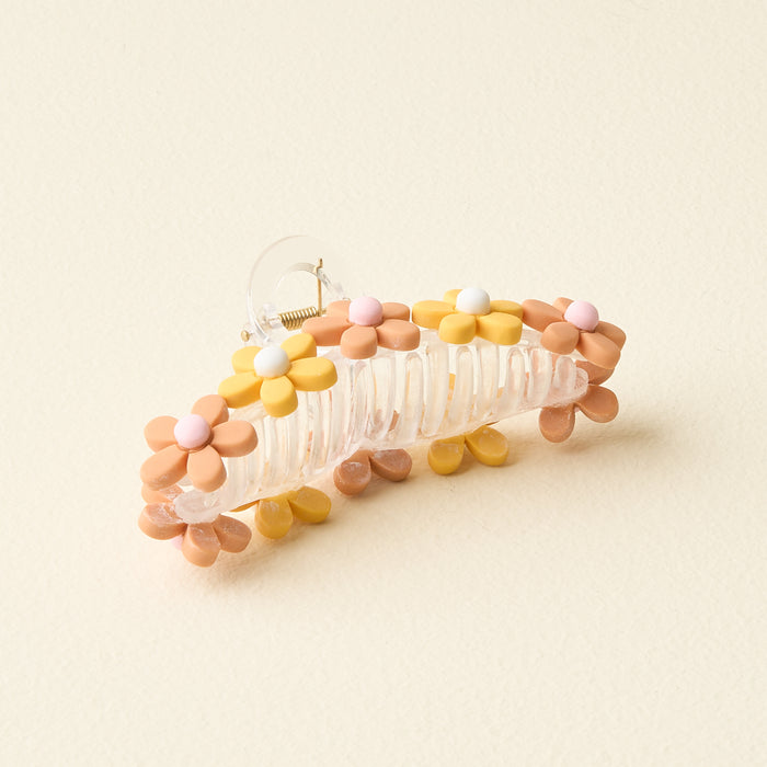 The Peachy Daisy Claw Clip by The Darling Effect is a transparent hair accessory featuring pastel flower designs in yellow, pink, white, and beige, shown on a light cream background.