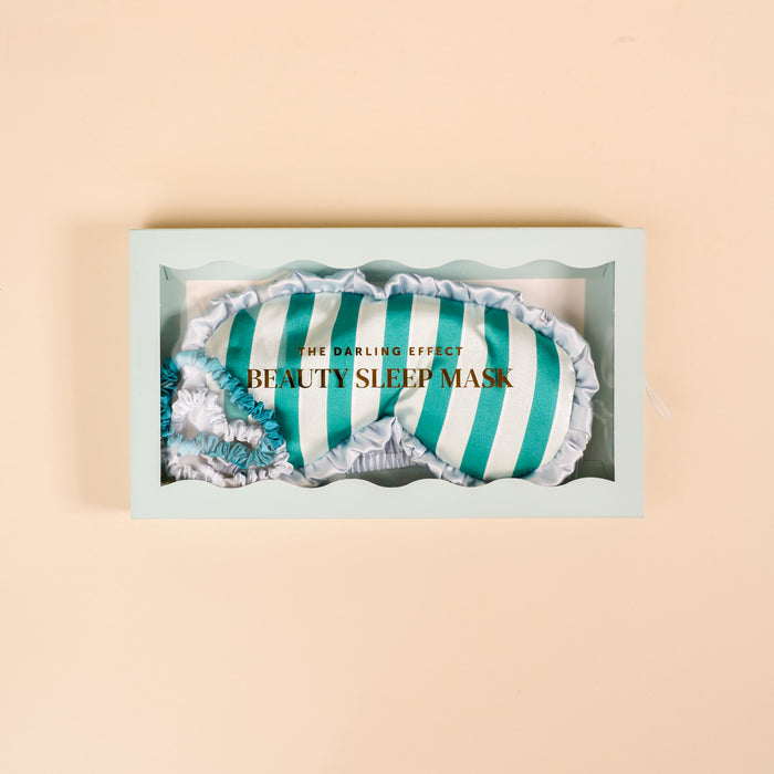 The Darling Effect Sicily Stripes Teal Beauty Sleep Mask features soft teal and white stripes with ruffled edges, displayed in a mint green boxβideal to pair with your favorite satin scrunchies or sleep set.