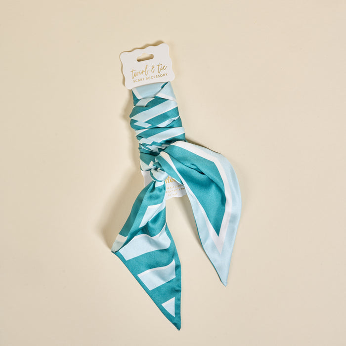 The Darling Effect's Sicily Stripes Teal Twirl & Tie Scarf Accessory, featuring teal and white stripes, is neatly tied at the center and displayed on a branded card against a beige backgroundβperfect for versatile outfit styling.