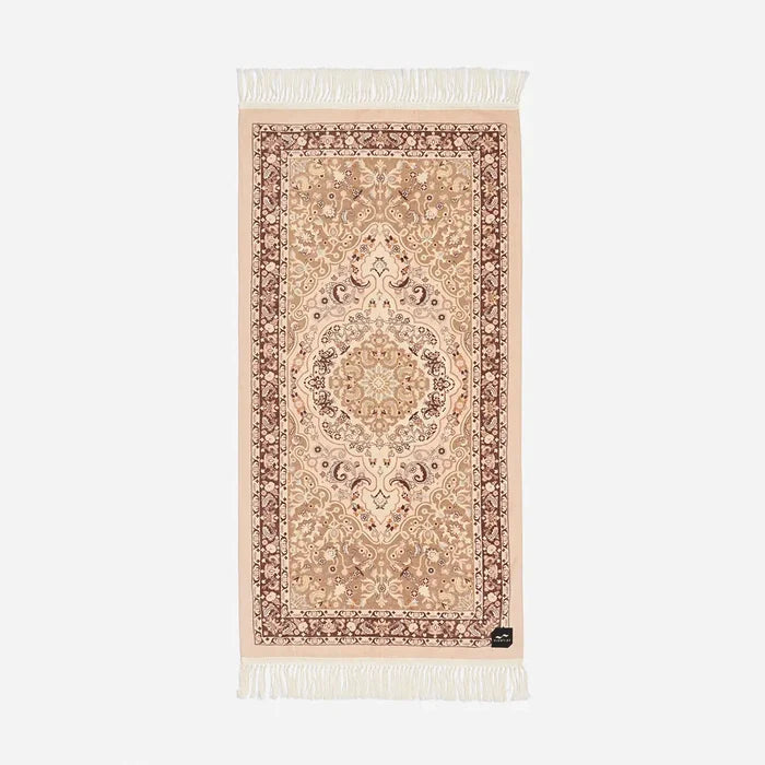 Slowtide Haven Beach Towel in Fawn features ornate central motif, floral border, and white fringe trim at both ends.
