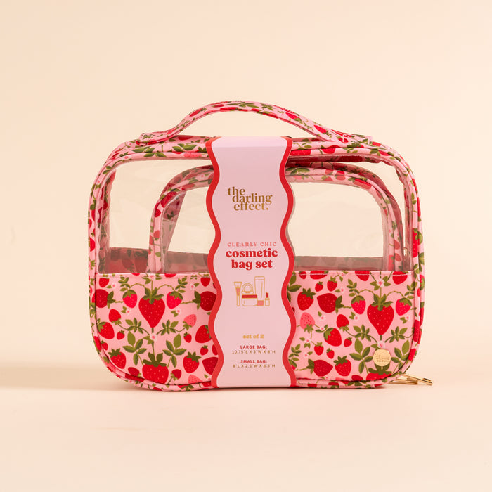 The Darling Effectβs Strawberry Fields Clearly Chic Cosmetic Bag Set includes two clear makeup bags with pink trim and a strawberry patternβideal as a travel toiletry duo.