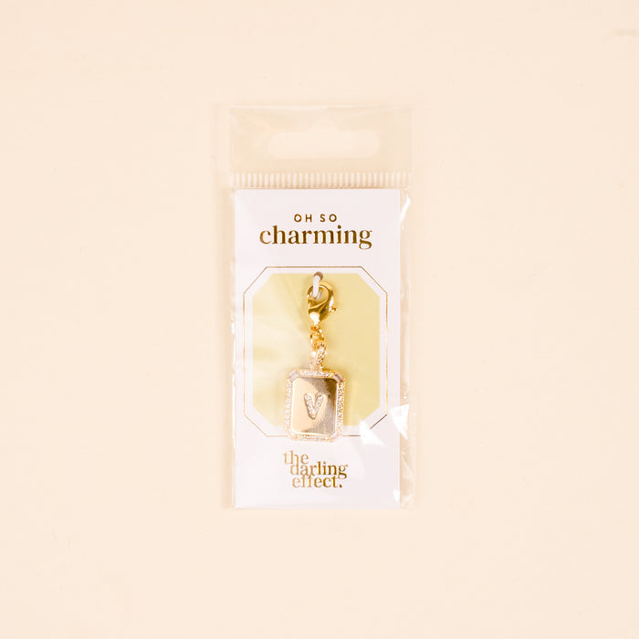 The-darling-effect's V Jewelry Charm Initial Letter Gold is a gold-plated rectangular pendant with the letter V, packaged in clear plasticβperfect for fans of personalized and Initial Letter Jewelry Charms.