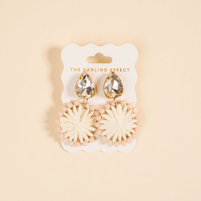 White Radiant Gem Earrings by The Darling Effect feature a raffia sunburst design with pink beads, presented on a branded card—perfect lightweight earrings for everyday wear.