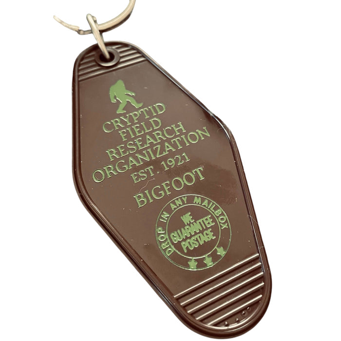 Forager Provisions LTD brown plastic motel key fob featuring a green Cryptid Field Research Org Bigfoot design.