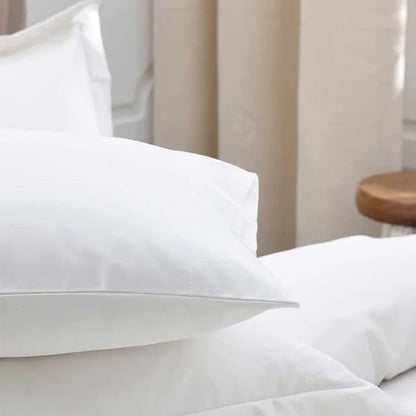 500TC Egyptian Cotton White Pillowcase on a bed with a neutral-colored curtain in the background.