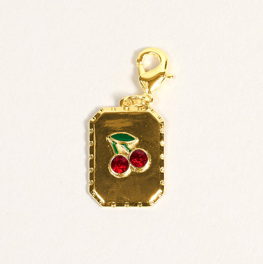 The Darling Effect's A Cherry Moment Jewelry Charm Gold features a gold rectangular pendant with a cherry design—two red gemstones as cherries, two green leaves, and a gold lobster clasp—perfect for your favorite jewelry or charm bar.