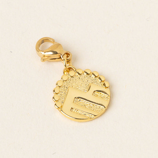 The Adventurous Jewelry Trait Charm Gold by the-darling-effect is a round gold charm with a lobster clasp, textured background, and raised stylized E, accented by small circles—symbolizing strength and confidence.