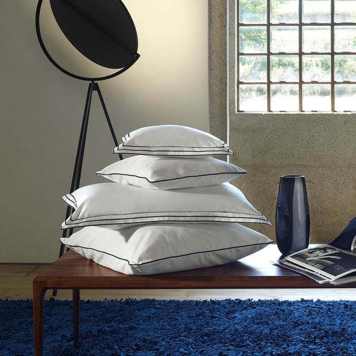 Stack of alba white black pillowcase sham on a wooden table in a room with a window and blue rug.