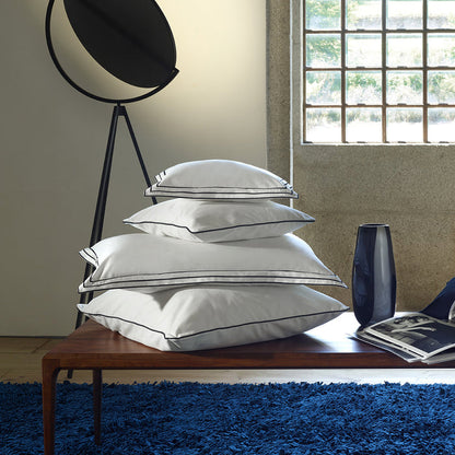 Stack of alba white black pillowcase sham on a wooden table in a room with a window and blue rug.