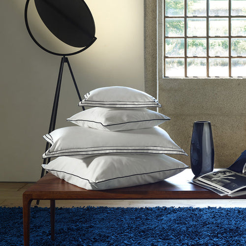 Stack of alba white black pillowcase sham on a wooden table in a room with a window and blue rug.