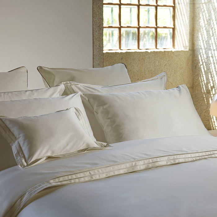 Neatly made bed with alba_white_sand_sham pillowcase and duvet cover in a bright bedroom.