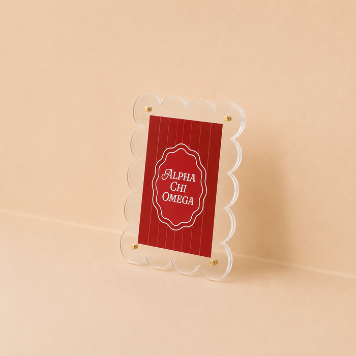 The Darling Effect’s Alpha Chi Omega Mini Acrylic Picture Frame Magnet features a scalloped-edge clear acrylic frame holding a red card with white “Alpha Chi Omega” text, displayed on a beige background.