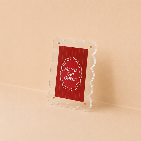 The Darling Effect’s Alpha Chi Omega Mini Acrylic Picture Frame Magnet features a scalloped-edge clear acrylic frame holding a red card with white “Alpha Chi Omega” text, displayed on a beige background.
