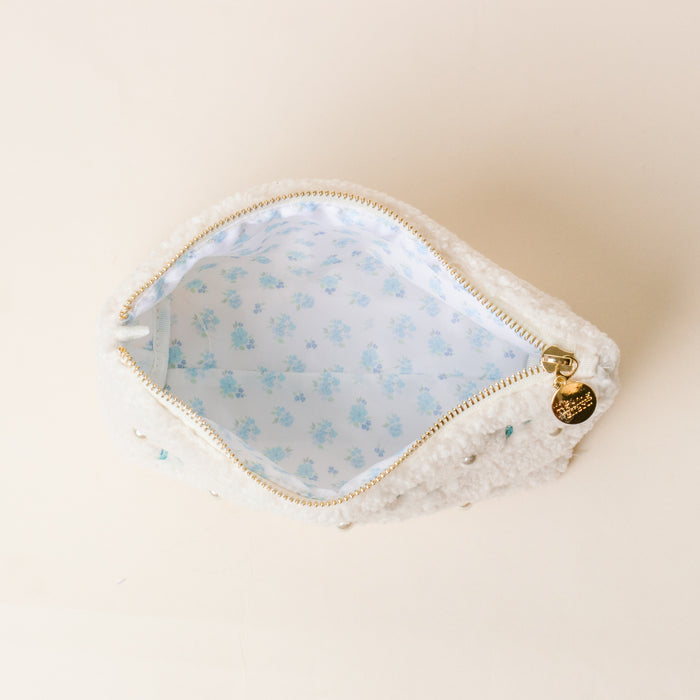 The Darling Effect’s Alpha Xi Delta Bows & Pearls Teddy Pouch features fluffy white sherpa, pearl accents, a gold zipper pull, and a light blue floral lining—perfect as a charming sorority gift.