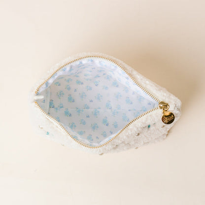 The Darling Effect’s Alpha Xi Delta Bows & Pearls Teddy Pouch features fluffy white sherpa, pearl accents, a gold zipper pull, and a light blue floral lining—perfect as a charming sorority gift.