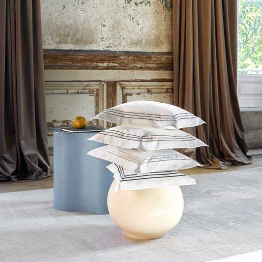Stack of alvorado pillowcases on a small table with curtains and a textured wall in the background