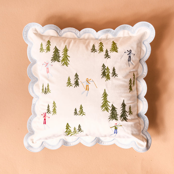 The Darling Effect's Aprés Ski Scalloped Square Throw Pillow features scalloped white edges and embroidered skiers and green trees, adding cozy lodge charm to your mountain retreat or après-ski décor.