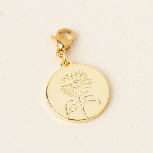 The-darling-effect's April Jewelry Birth Flower Charm Gold is a round gold charm with a lobster clasp and engraved sunflower, perfect for birth flower enthusiasts or as a meaningful accessory.