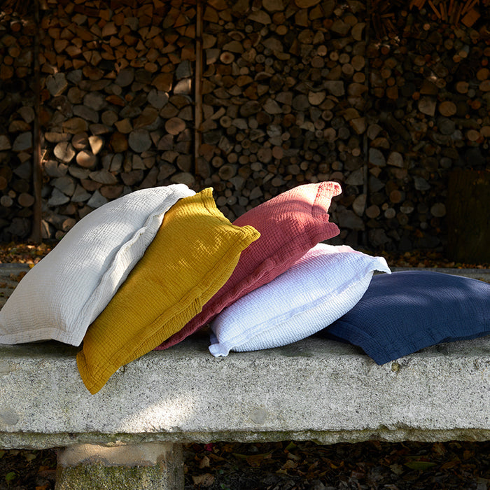 Areia saffron white and terracotta decorative pillowcases stacked on a stone ledge with a wooden log pile background