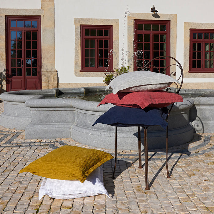 Areia terracotta white and saffron decorative pillowcases on a stand in front of a building with red doors and windows.