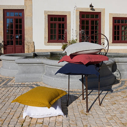 Areia terracotta white and saffron decorative pillowcases on a stand in front of a building with red doors and windows.