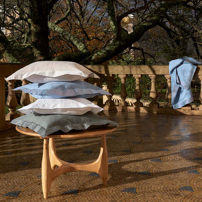 Stack of Aura trivoli and pewter decorative pillowcases on a wooden stool with a scenic background