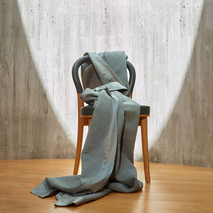 Aura-Pewter bedspread draped over a chair against a neutral background