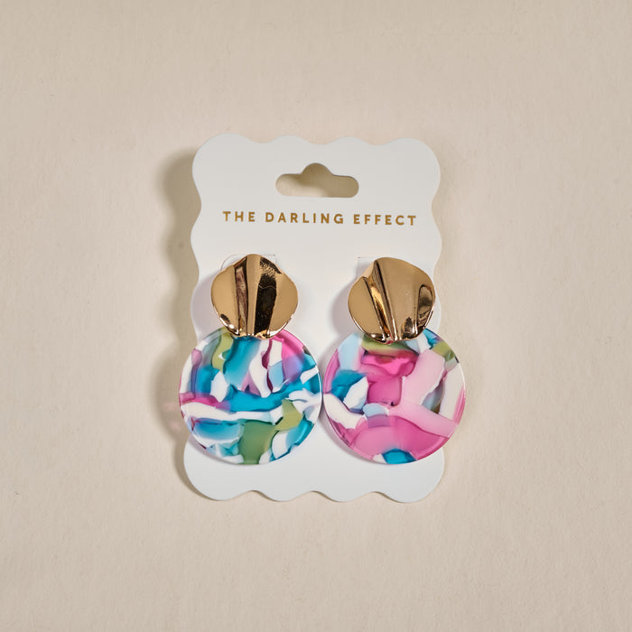 The Darling Effect Aurora Marble Muse Earrings feature gold-tone tops and large, round drops with a colorful marbled pattern in pink, blue, white, and green, displayed on a branded card.