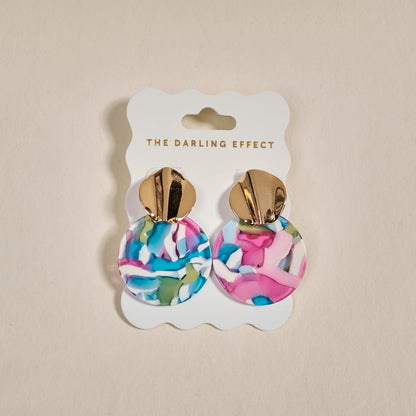 The Darling Effect Aurora Marble Muse Earrings feature gold-tone tops and large, round drops with a colorful marbled pattern in pink, blue, white, and green, displayed on a branded card.