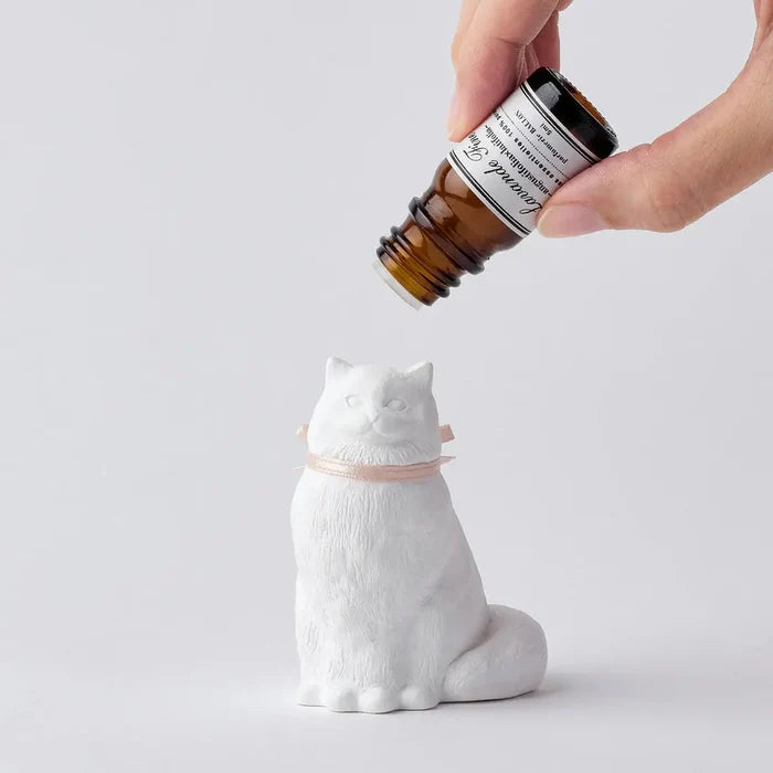 Hand pouring oil onto Ballon Chiffon Cat Plaster Aroma Diffuser, handcrafted in Tokyo, minimalist background, home fragrance.