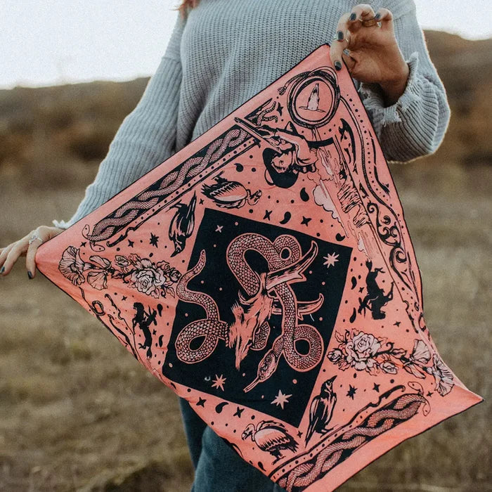 Person holding Rattle & Hiss Bandits Bandana, orange organic cotton square, outdoors. Eco-friendly bandana accessory.